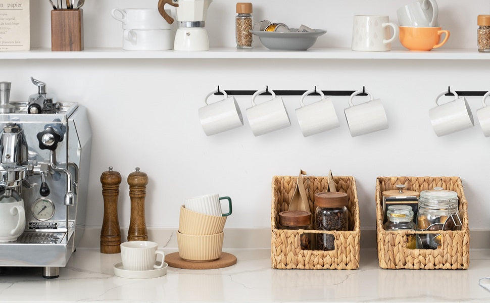 Two water hyacinth storage baskets with built-in handles on a kitchen countertop, holding coffee jars and pantry items