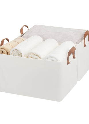 White storage bin with brown PU handles containing folded clothes on a white background