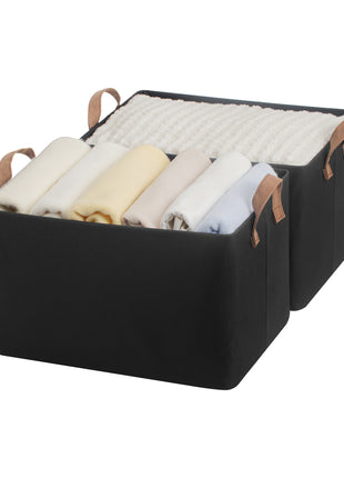 Black storage basket with brown handles filled with folded clothes on a white background