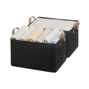 Black storage basket with brown handles filled with folded clothes on a white background