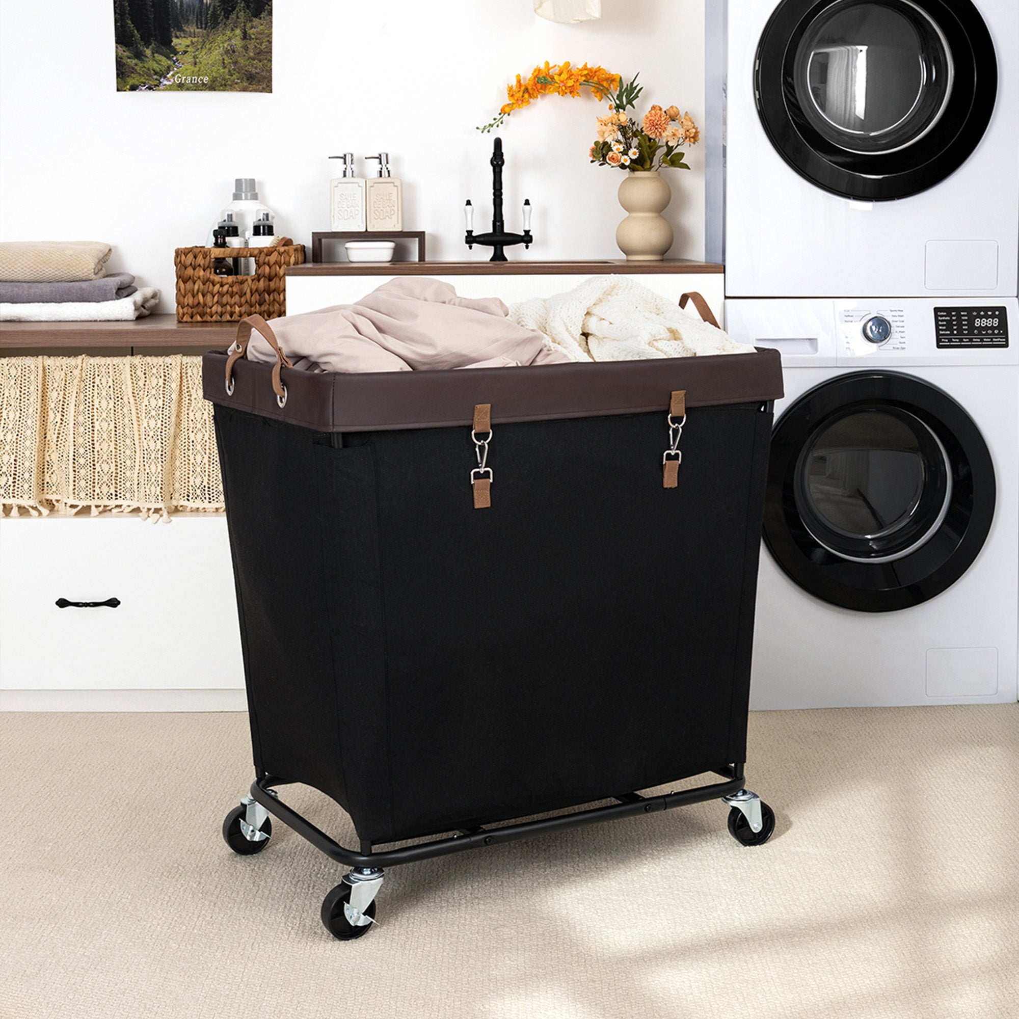Large rolling laundry basket with wheels, black fabric, brown leather straps, metal frame, in front of laundry machines.